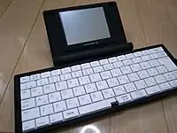 ポメラの写真。折り畳み式のキーボードと、その奥に配された液晶ディスプレイを含む本体からなる。形状はノートパソコンに似る。展開時のキーボードの横幅は本体の2倍近い。