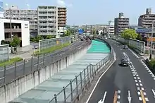 半地下区間の地上側(画像左)と専用部(画像右)。左画像:一般部の中央に半地下区間の開口部がある。当初は地階の高速道路が見えたが騒音対策のために蓋が取り付けられた。右画像:ドライバーの心理的圧迫感を取り除くため構造物に丸みを付けた。