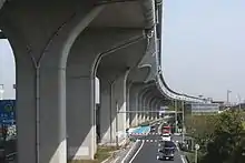 環状2号のPC連続ラーメン橋(左)と標準的なT字型橋脚の高架橋(右)。T字型では梁があるために道路長手方向の連続性が損なわれ、美的観点から好ましくないとされた。美的に良くないことは、用地買収を行うにあたって拒絶反応を示されかねないため、その対策としてPC連続ラーメン構造を採用することになった。