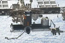 雲に覆われた地球を背景にした「きぼう」日本実験棟とHTV（こうのとり）の進行方向側側面
