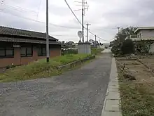 日鉱本幸崎駅跡（写真中央）国鉄バス「本幸崎」であったバス停は大分バス「神崎中学校」に変更されている。かつては見通しの良い直線であった線路跡も、国道197号のバイパス道路によって視界を絶たれてしまっている。