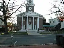 The front façade of a nineteenth-century brick church building with columns and Greek Revival pediment, cupola, and steeple