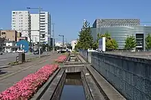 福井県福井市を流れる芝原用水（芝原上水）。右前は福井県国際交流会館。（福井市、北緯36度4分1.58秒 東経136度13分35.09秒﻿ / ﻿北緯36.0671056度 東経136.2264139度﻿ / 36.0671056; 136.2264139﻿ (福井市を流れる芝原用水)）