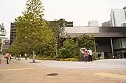 北西端の交差点歩道の上から望むグランドプラザとイベントホール。左側の樹木に隠された黒い建物がグランドプラザ、右側の低層建物がイベントホール