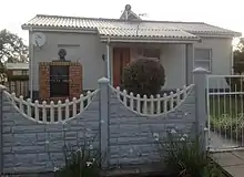 小さな、1階建ての戸建て住宅。壁は薄い青色、屋根は波型の鉄でできている。