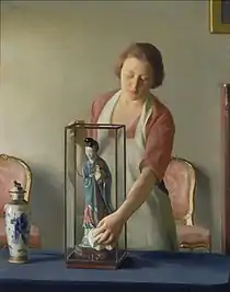 磁器製の人形(豆像)を納めたケースを掃除する女性を描いた1921年の油彩画。