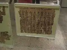 博物館にて厚いガラスで密閉して展示されている古いパピルス断片。黒いインクを用い、ヒエラティックで手書きされている