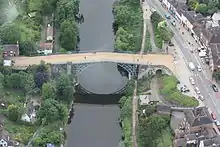 橋の航空写真。川沿いを走る幹線道路がすぐそばを通り、多くの建物がすぐ近くに点在することがわかる。
