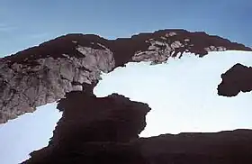 山頂と山腹が黒い岩で覆われた岩山。黒い岩と氷河の氷の斑点が全景を覆う。