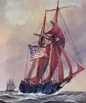 A two-masted wooden sailing ship is shown in full sail on the sea.  It is flying the flag of the United Colonies: thirteen red and white stripes, with a British Union Jack in the upper left quadrant.  Another ship is visible in the distance.