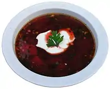 サワークリームとパセリの葉を添えた、濃い赤色のボルシチが装われたボウル