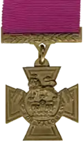 A bronze cross pattée bearing the crown of Saint Edward surmounted by a lion with the inscription "FOR VALOUR". A crimson ribbon is attached.
