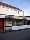 白い塀の付いたピンク壁・赤屋根の店には「セント・ジョージズ・ニュース」との文字が書かれている