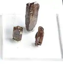 白い背景の上の三つの柱状をした茶色の結晶